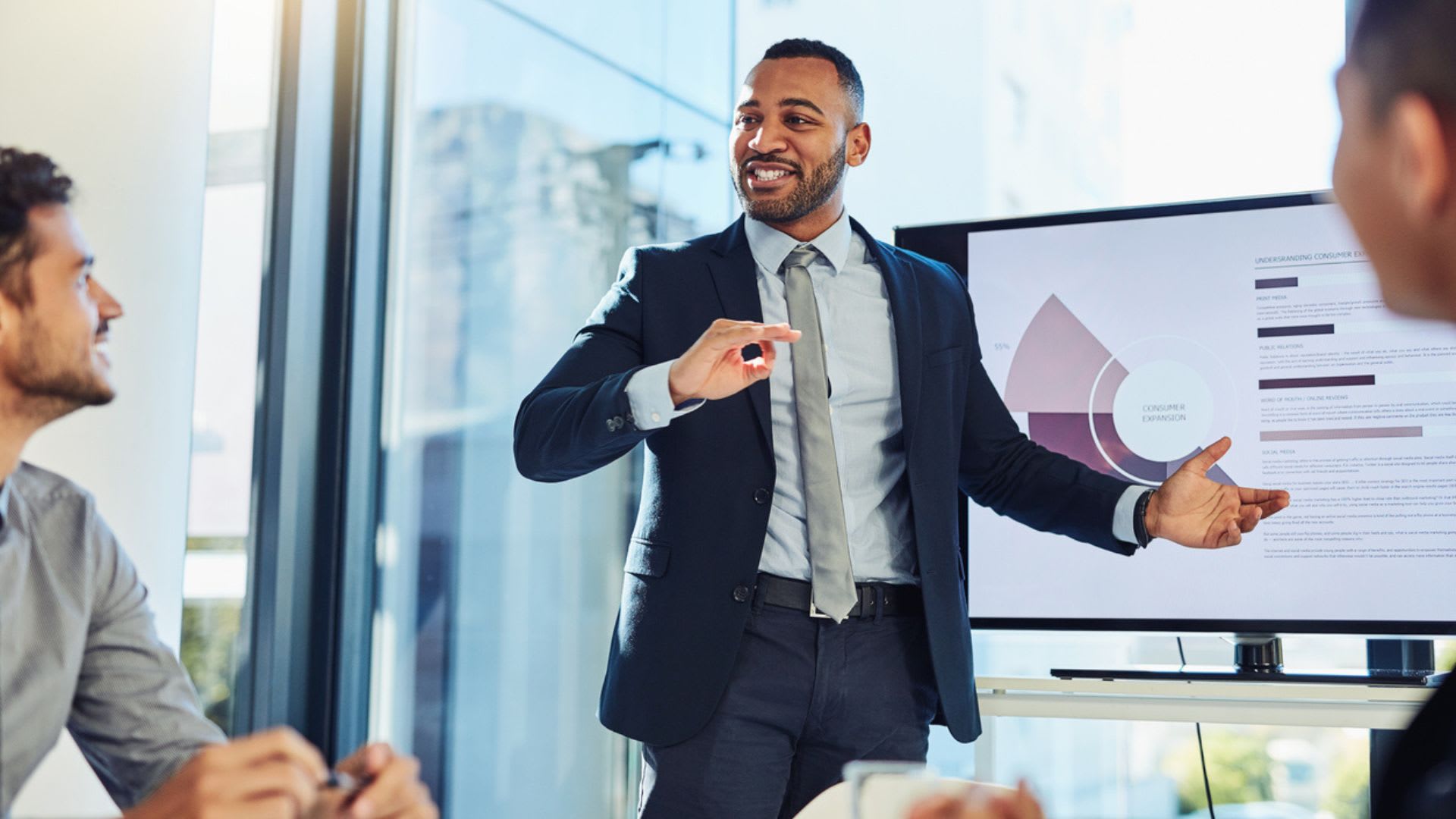 A professional man in a suit presenting to his colleagues in a meeting room.