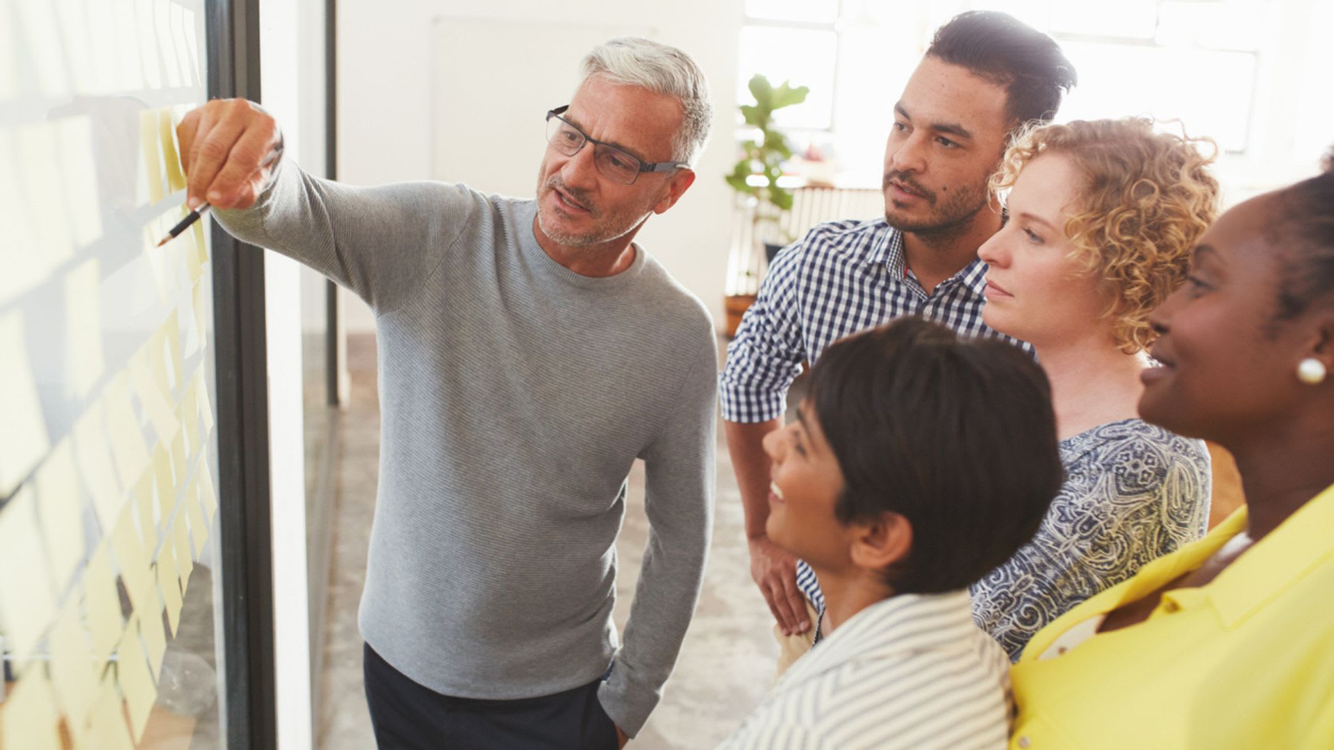 People in a workplace setting observing a group of notes displayed on a wall.