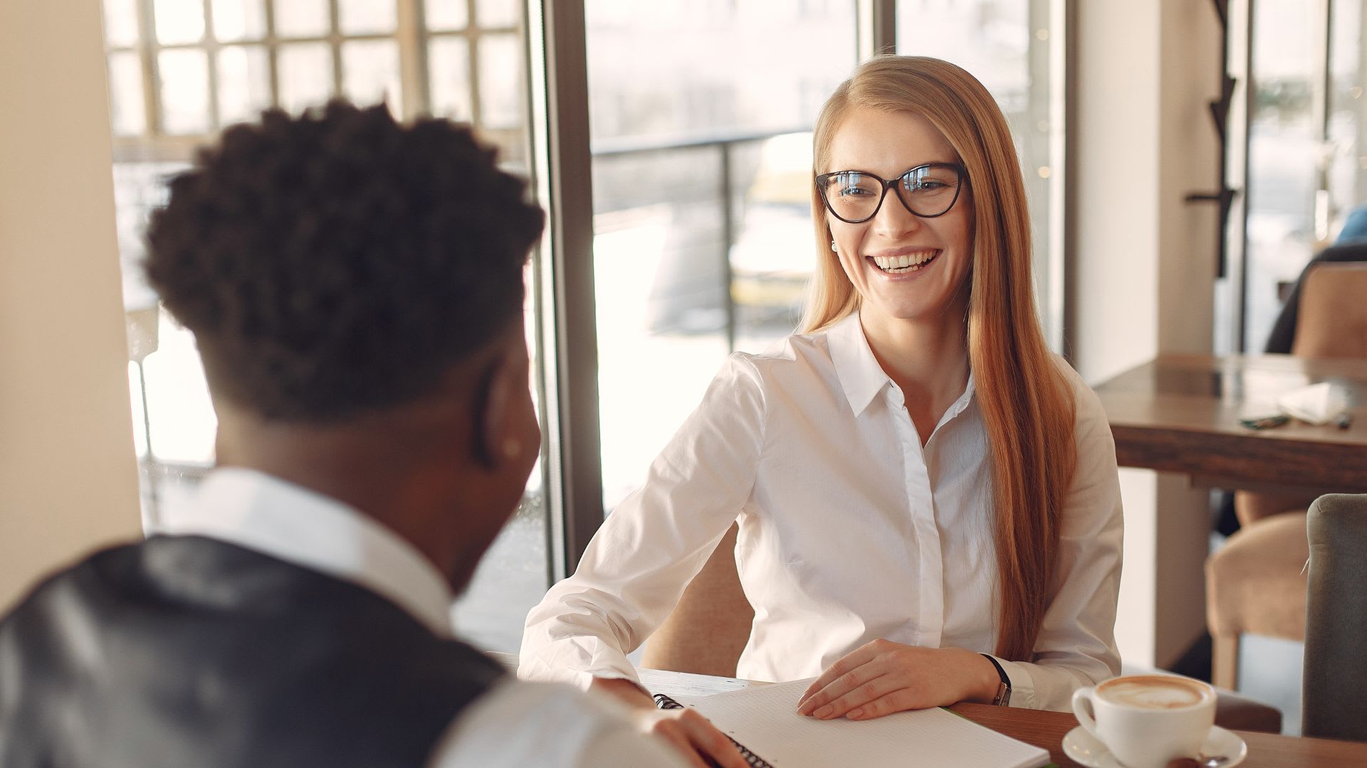 A woman with glasses converses with a man at a table, showcasing an interactive and engaging discussion.