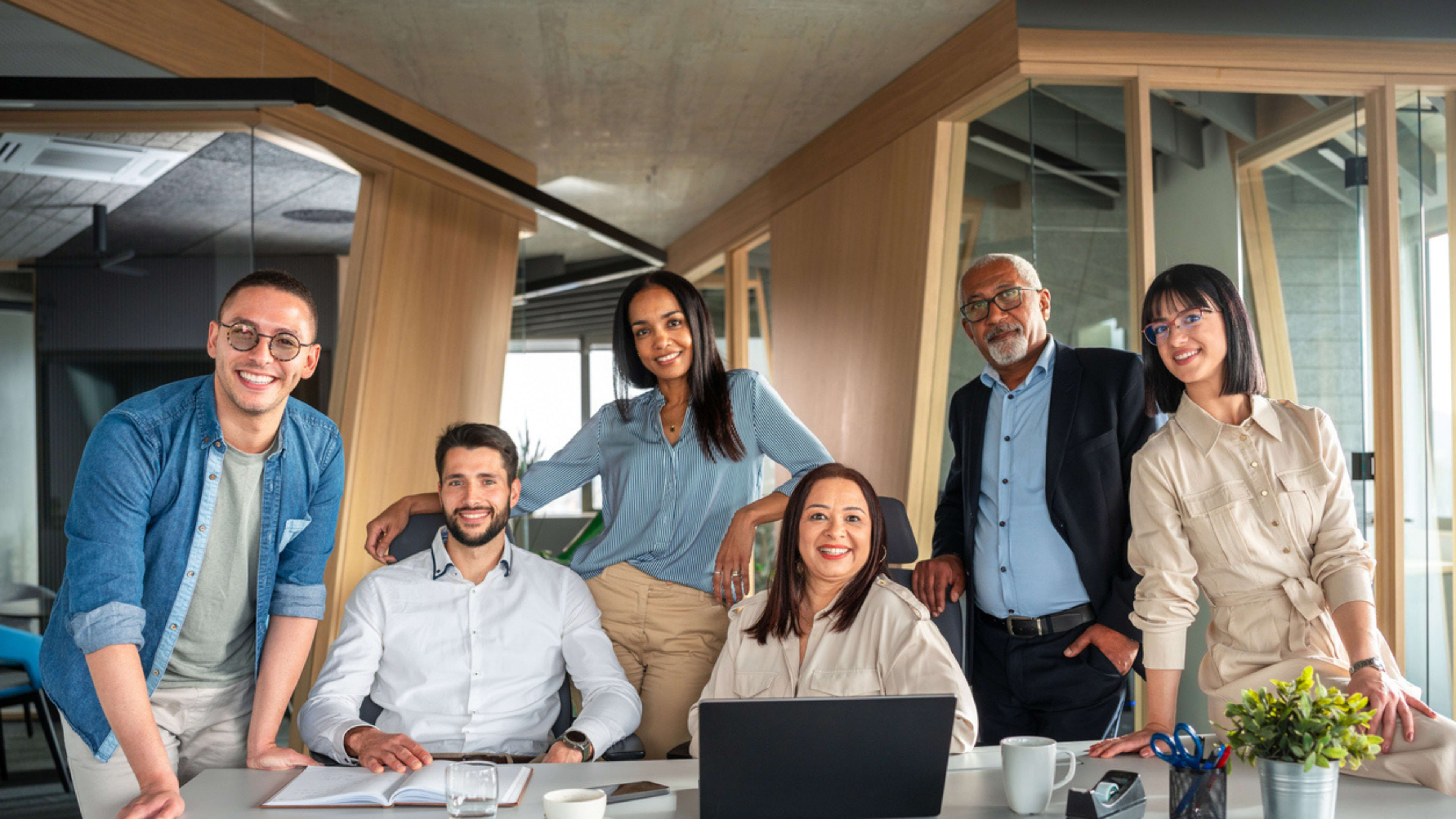 A team of colleagues standing together, smiling for a group photo in a well-lit office environment.
