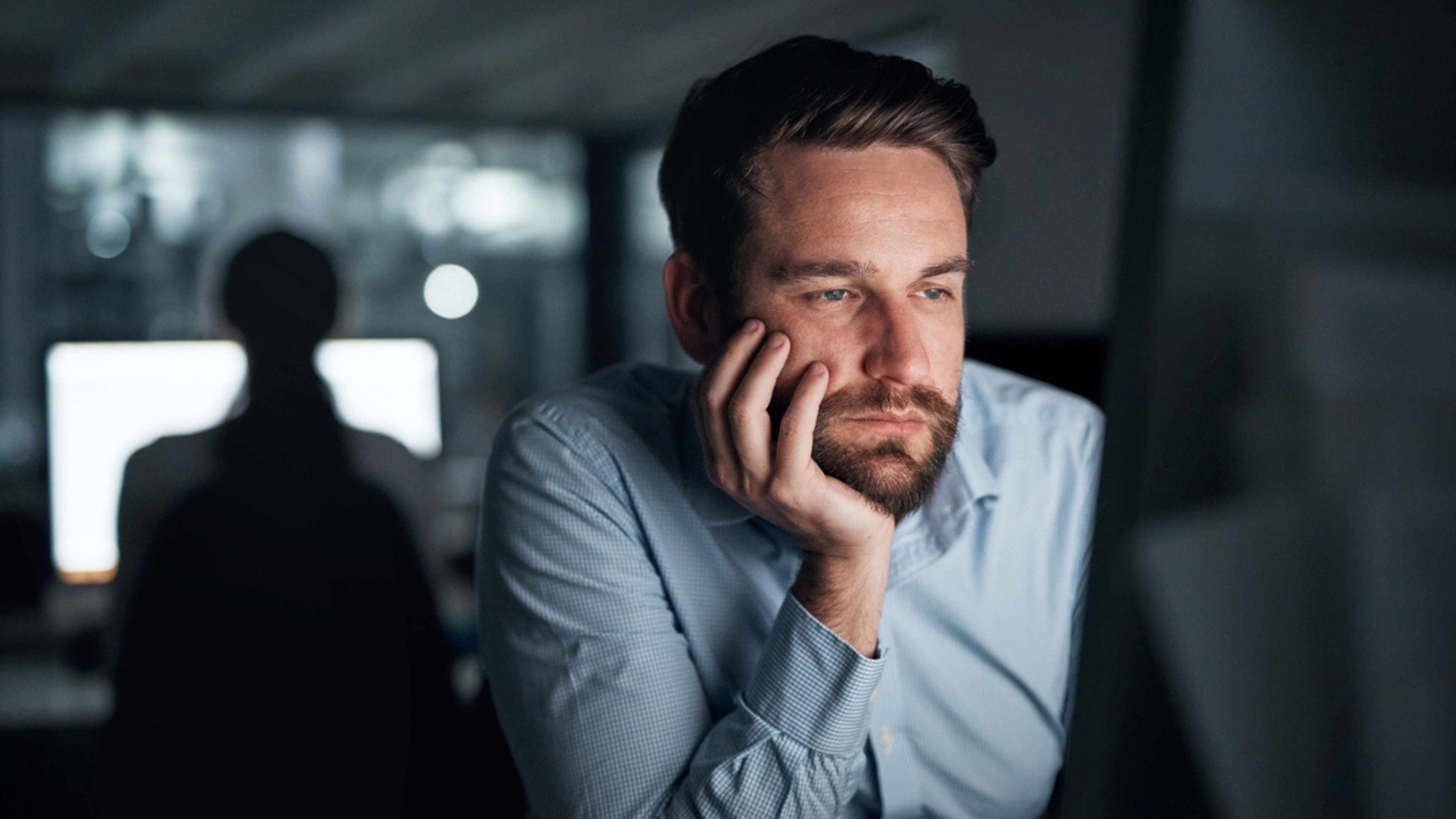 A man in a professional setting, sitting in front of a computer screen, looking bored or disengaged with his work. 