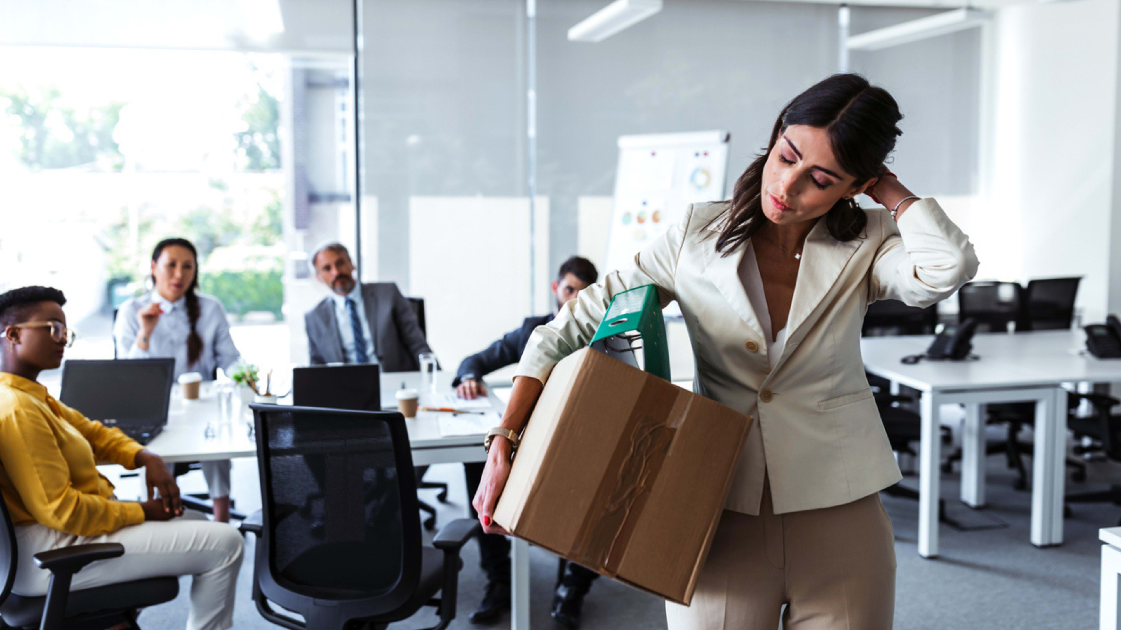 A woman in an office setting is carrying a box with her workplace belongings, showing that this is her last day working at the company. 