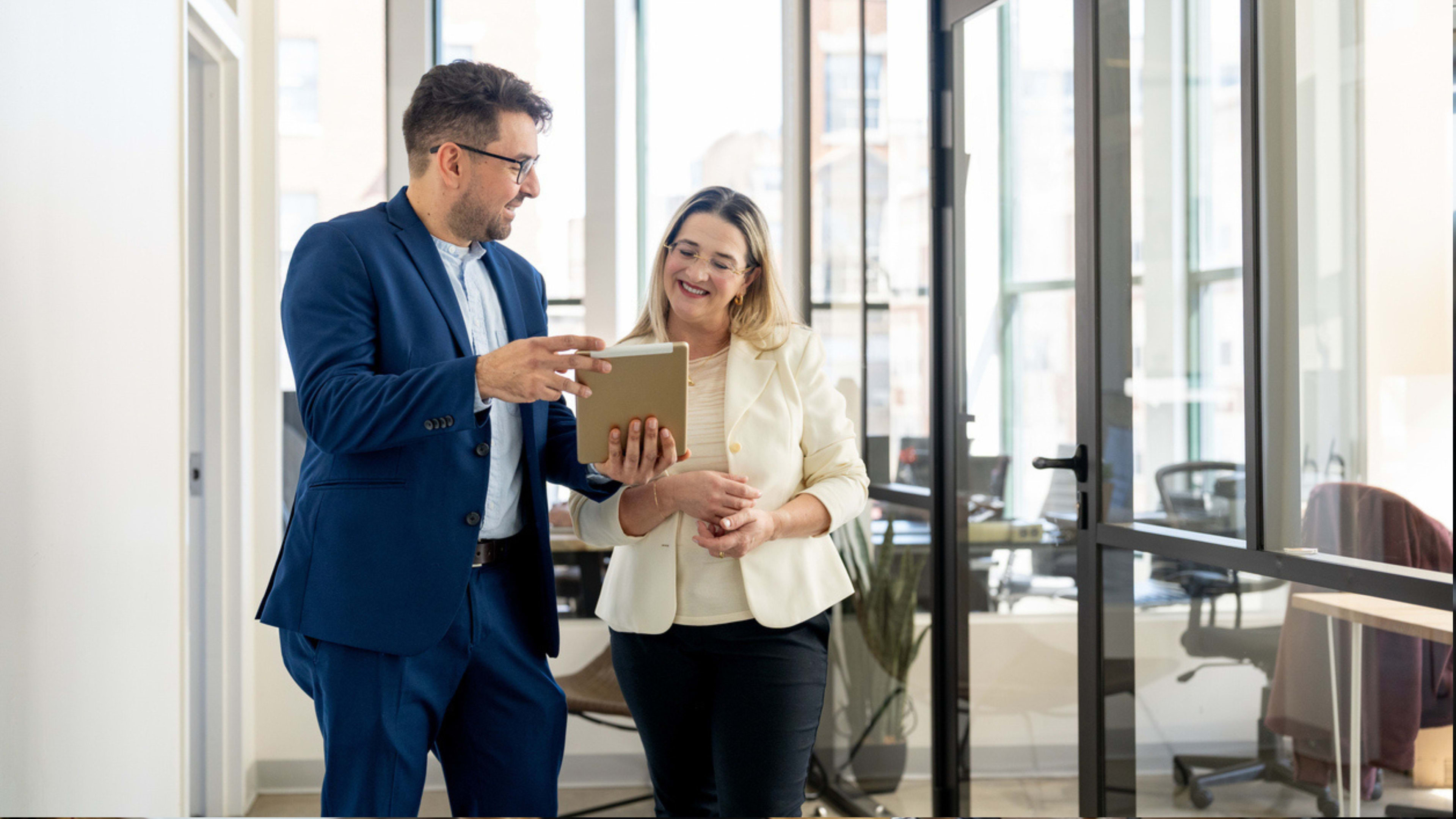 A man and woman walking through a hallway in an office setting looking over a document. 