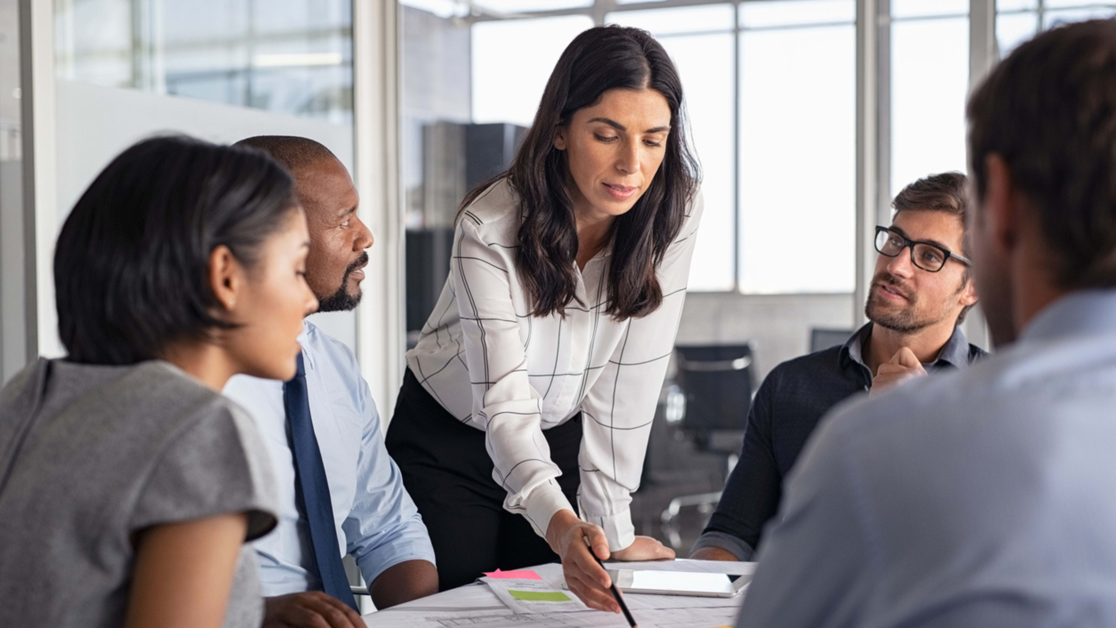 A woman stands at the head of a conference table during a collaborative work meeting. 