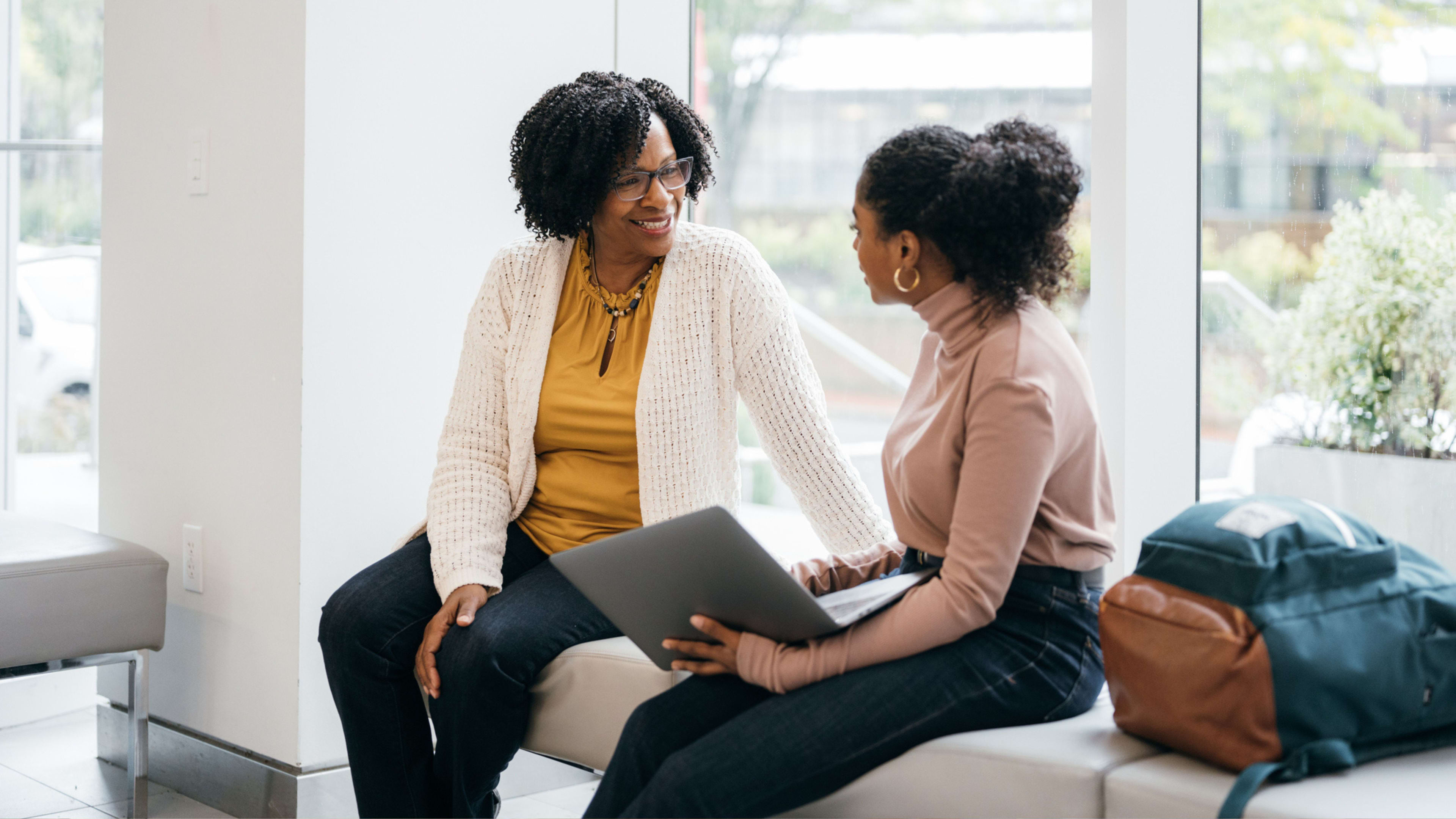 Two women engaged in conversation while sitting on a bench, using a laptop for their discussion.