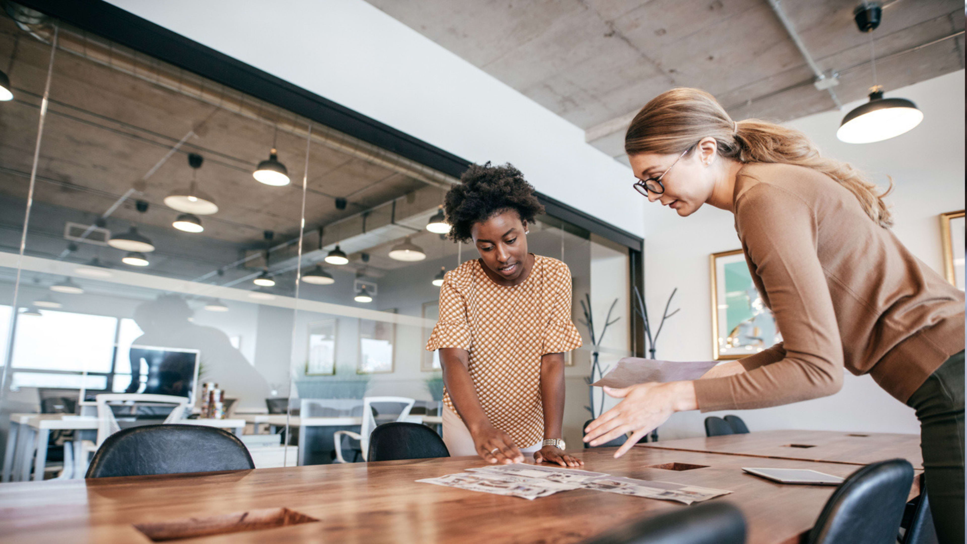 Two women collaborating on a project in a modern office setting, focused and engaged in their work.