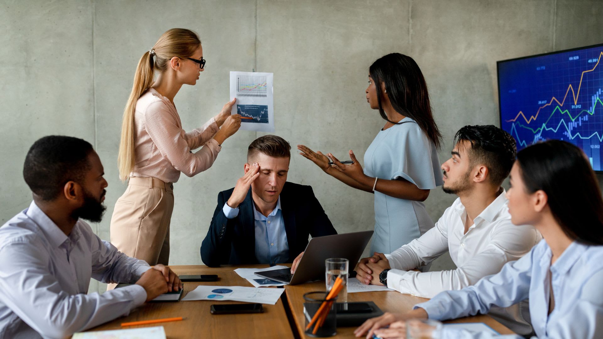 A group of business professionals engaged in a tense discussion within a modern meeting room setting.