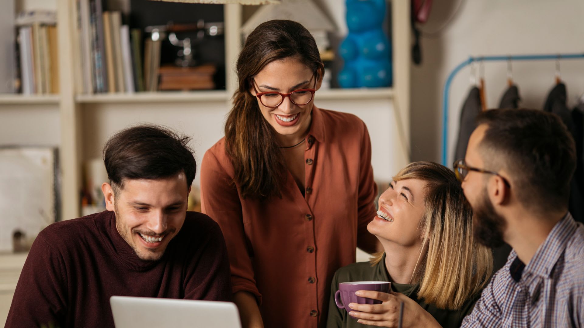 A diverse group of individuals smiles while gathered around a laptop, sharing a moment of joy and collaboration.