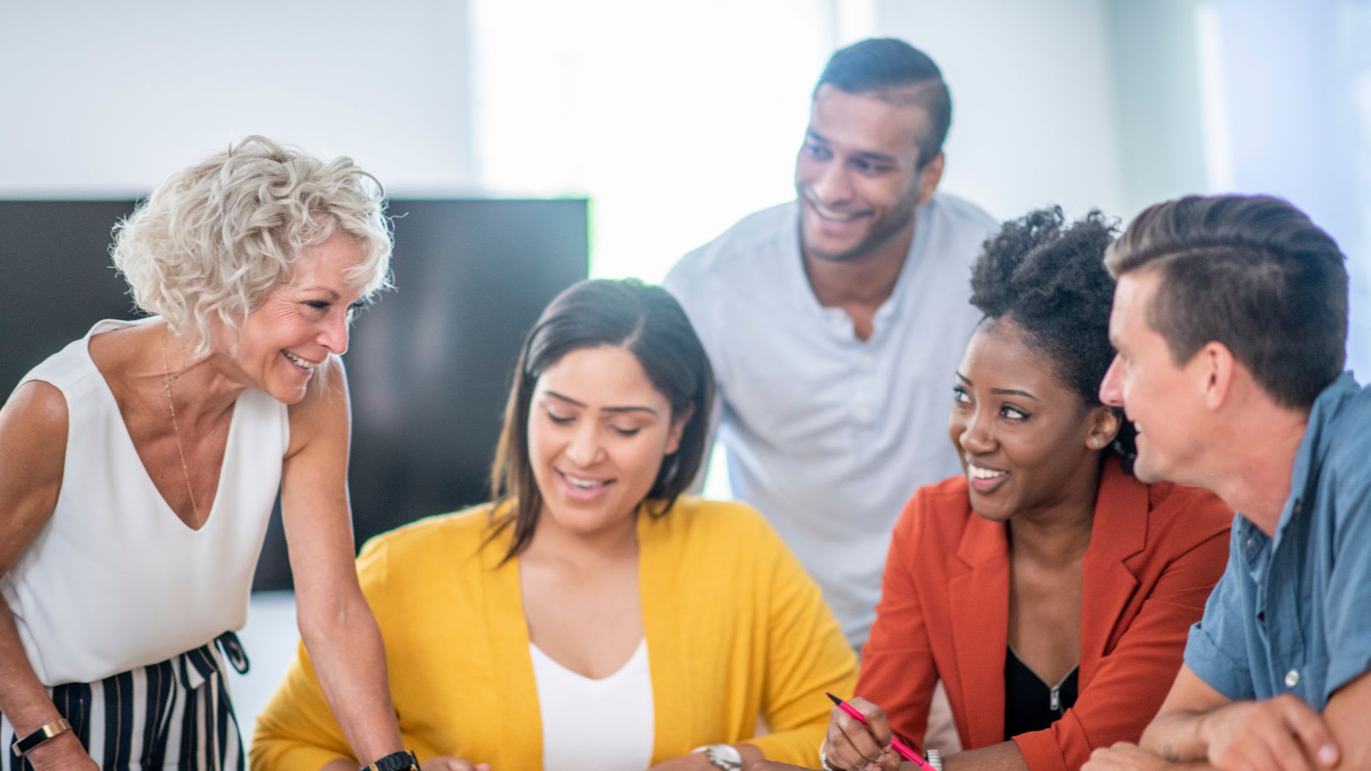 A cheerful group of people engages with a laptop, smiling together in a moment of connection and teamwork.