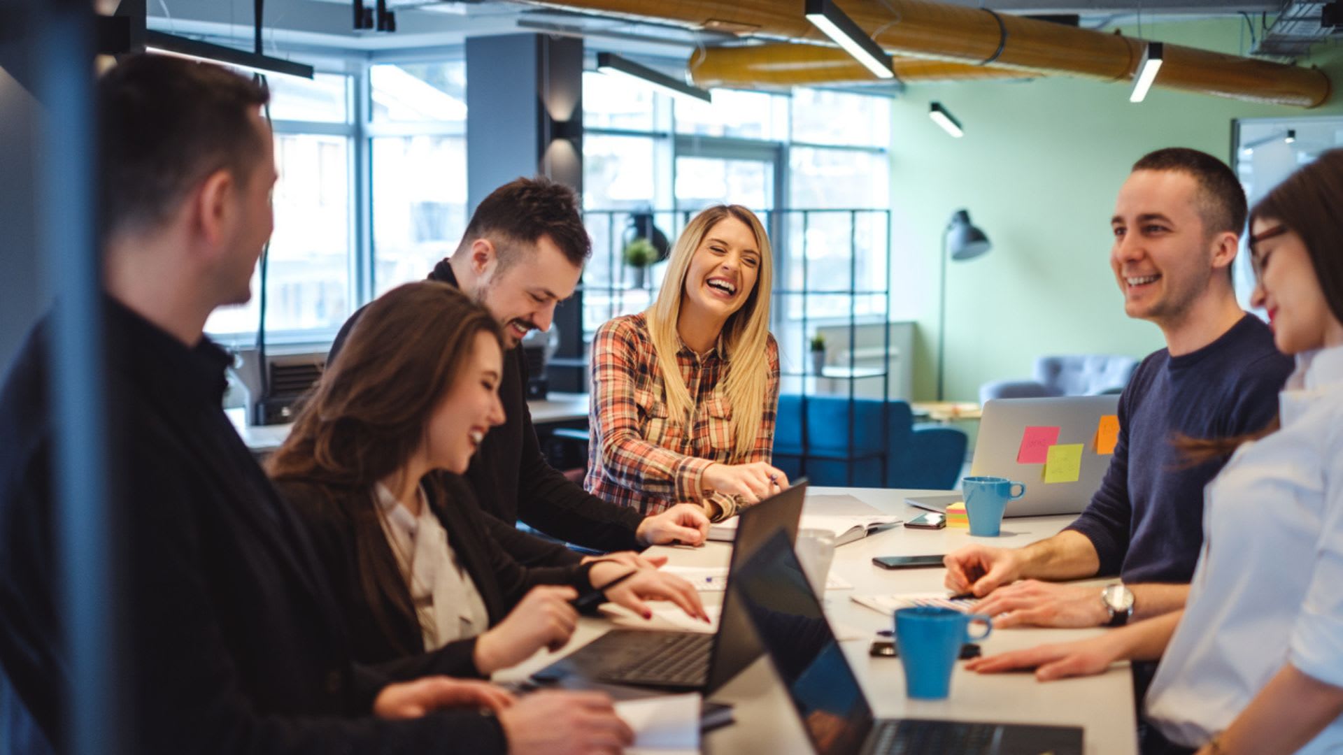 Happy colleagues laughing in the office at the meeting table.