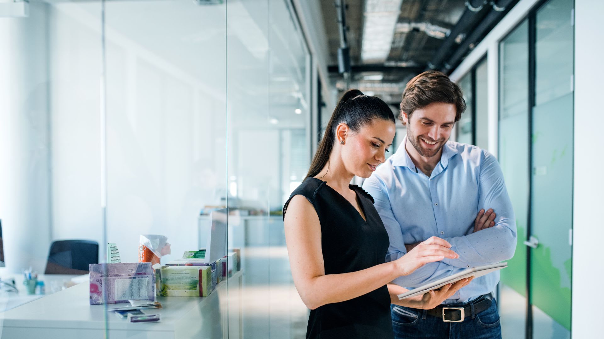 Two people in an office setting focused on a tablet, likely sharing information or working on a 