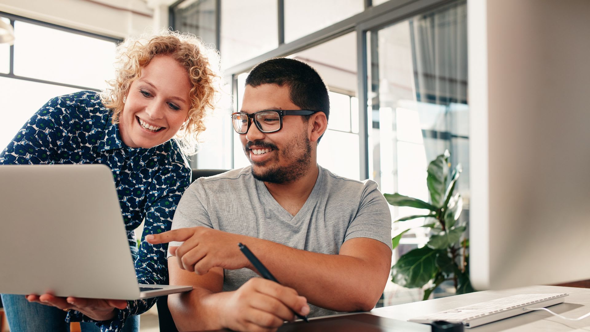 A man and woman focus on a laptop screen, engaged in discussion and sharing ideas in a professional environment.