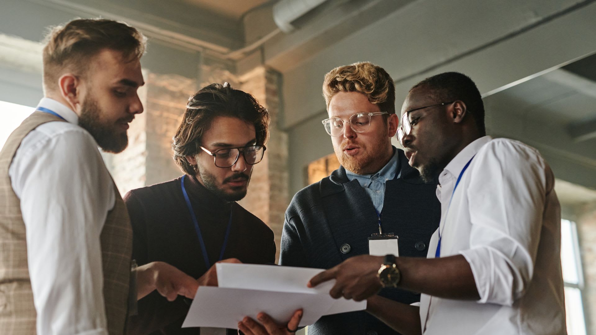 Four men gather around a table, intently examining a document laid out before them.