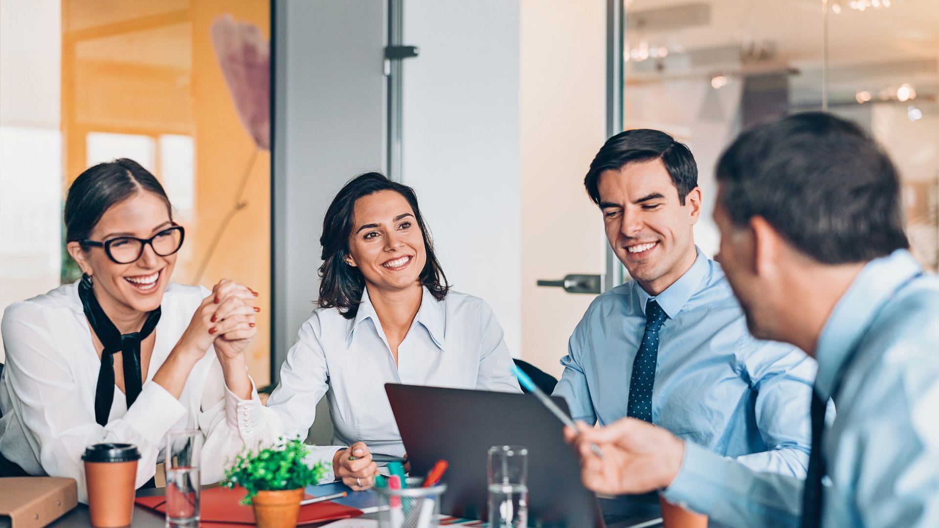A group of four business individuals collaborating at a table, utilizing a laptop for their meeting.