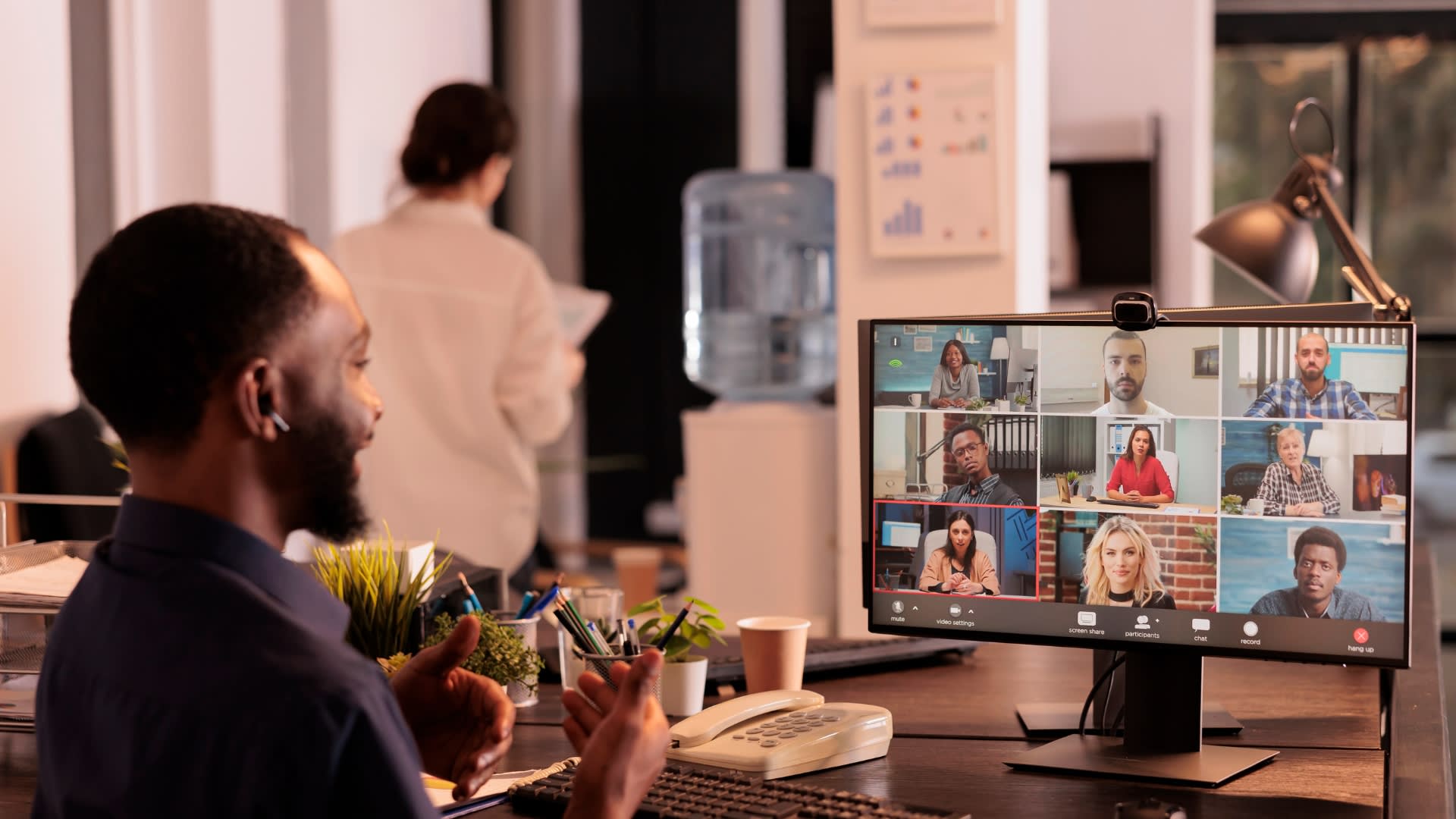 A man seated at a desk, engaged in a video conference displayed on his computer screen.