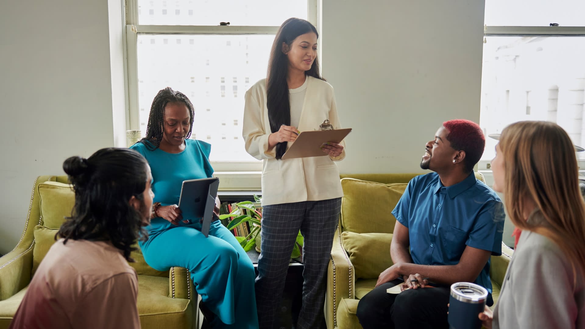A woman engages a group of colleagues in discussion within a modern office setting.