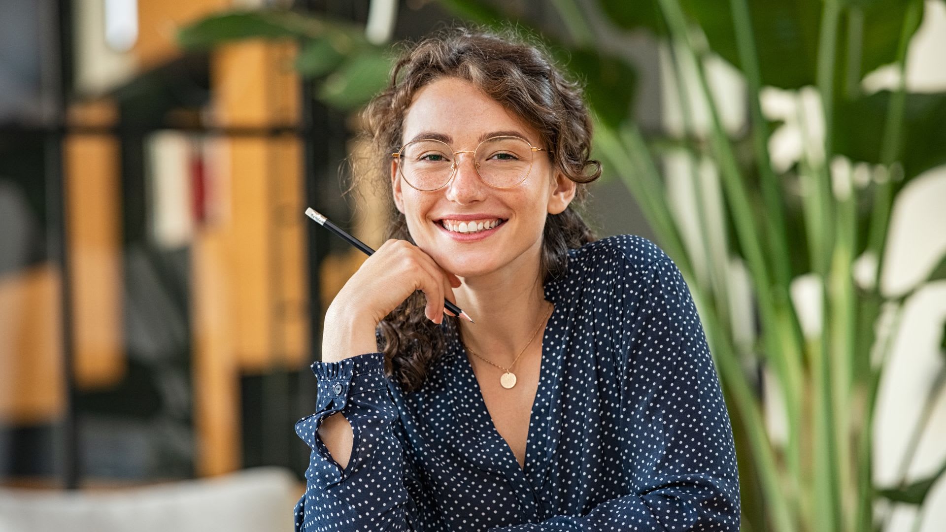 A smiling woman wearing glasses and a polka dot shirt, exuding warmth and positivity.