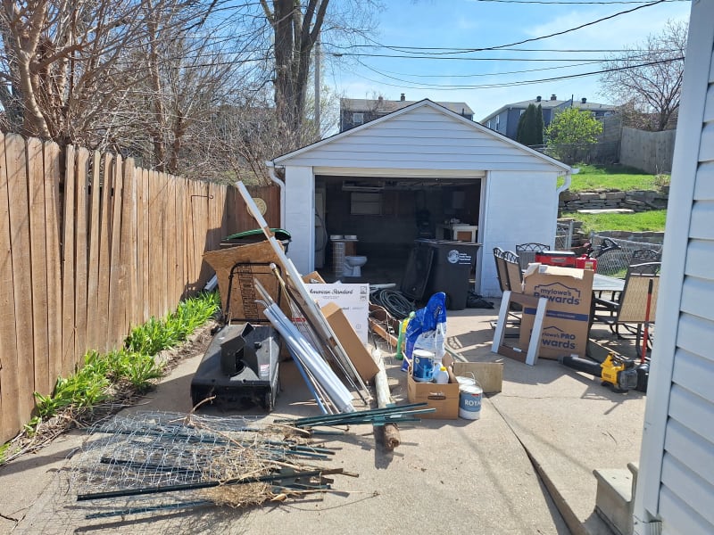 Garage and driveway full of junk including boxes, paint cans, and lumber before cleanout by A1 Junk Removal in Omaha, NE