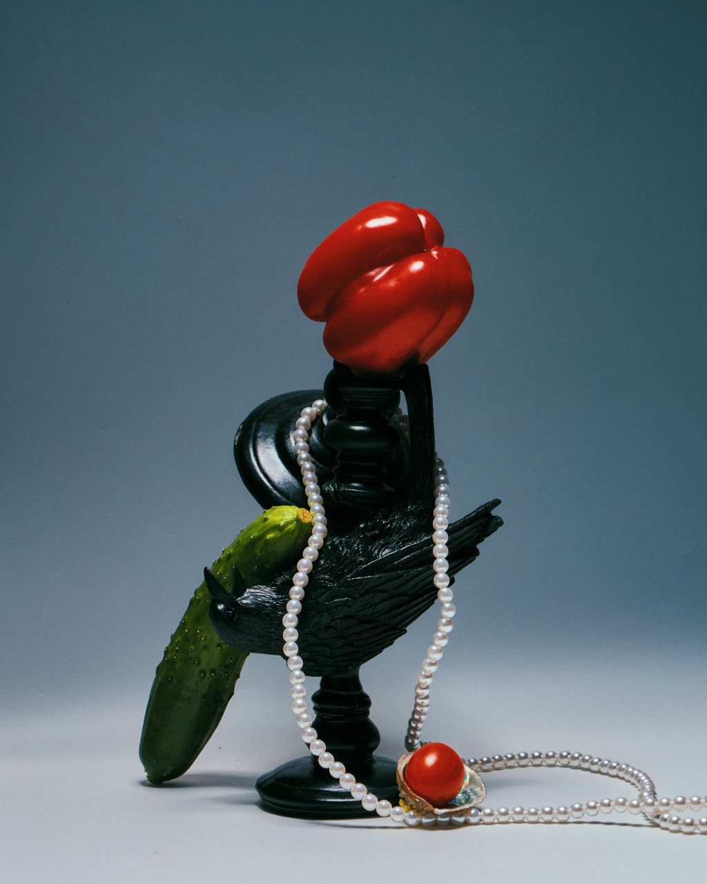 Sculptural product still life with red peppers, a black bird, cucumber, and pearls