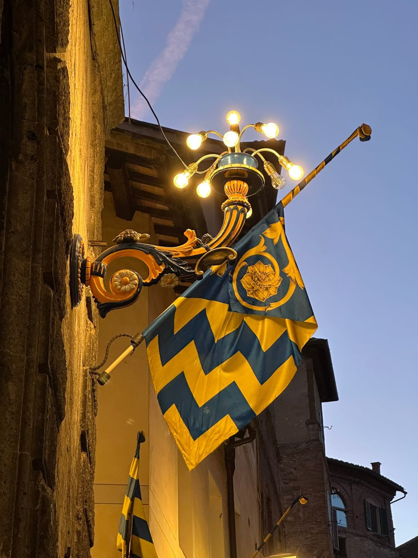 A contrada flag and wrought-iron lamp at dusk in Siena