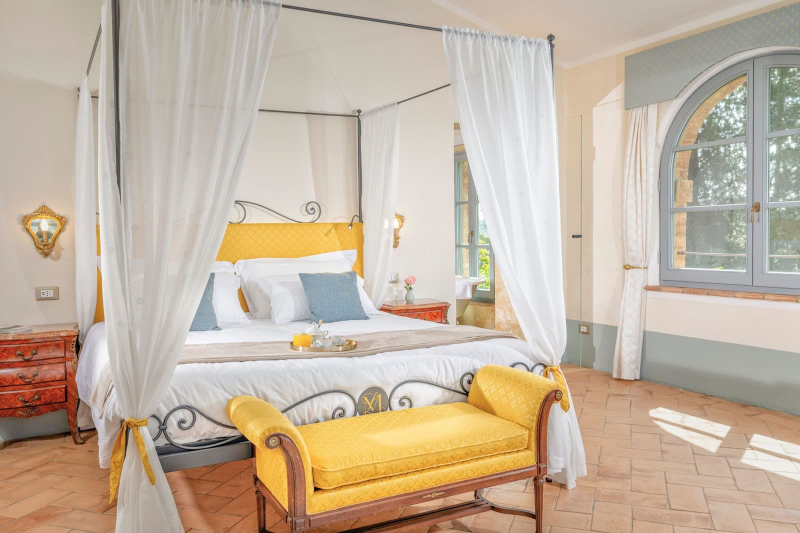 Villa Poggio d'Oro — a white canopy bed with a yellow velvet bench