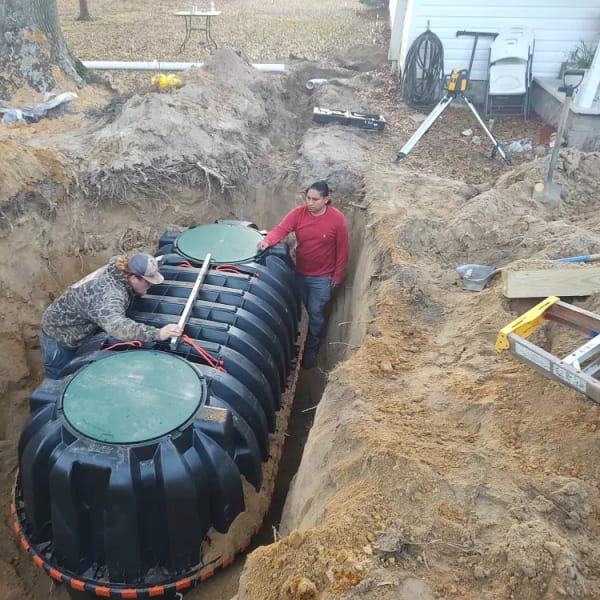 Crew setting a new two-chamber septic tank into an excavated trench in a back yard