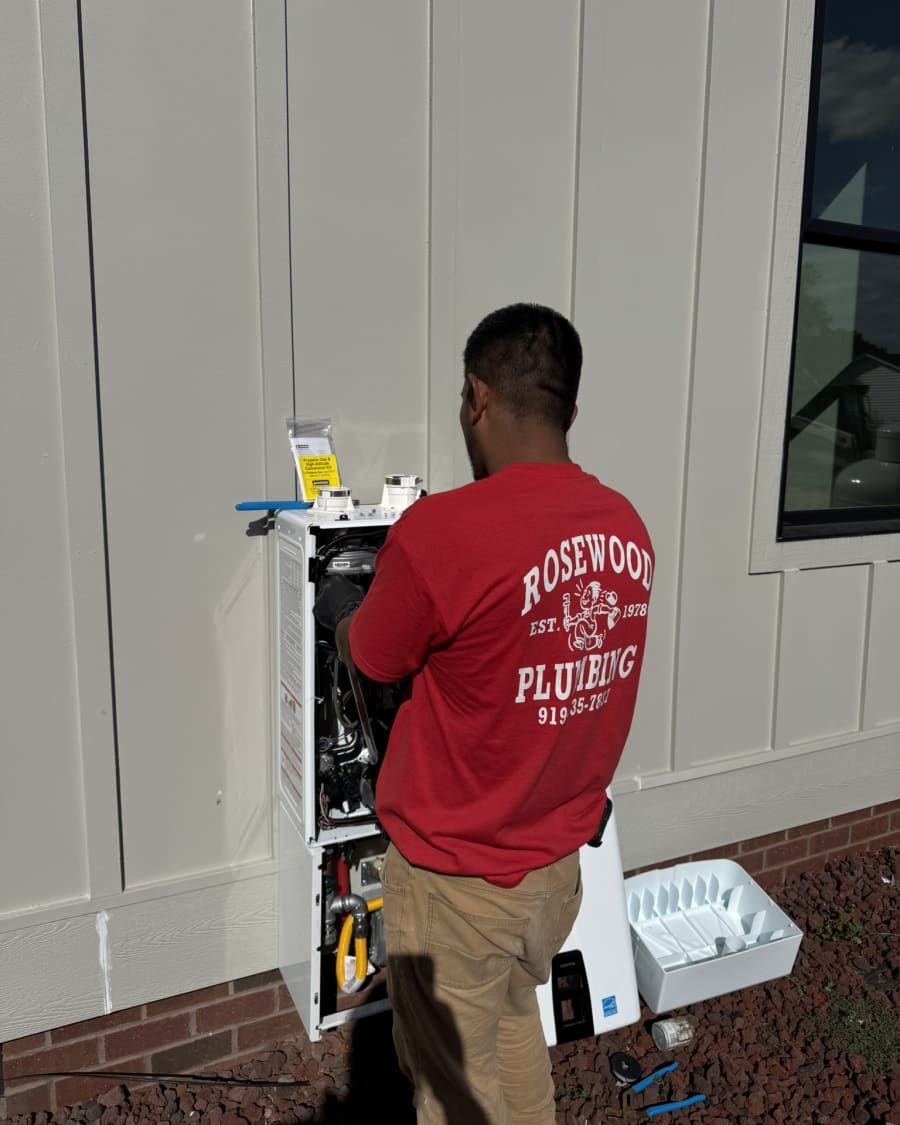 Rosewood Plumbing technician installing a tankless water heater on the exterior wall of a home