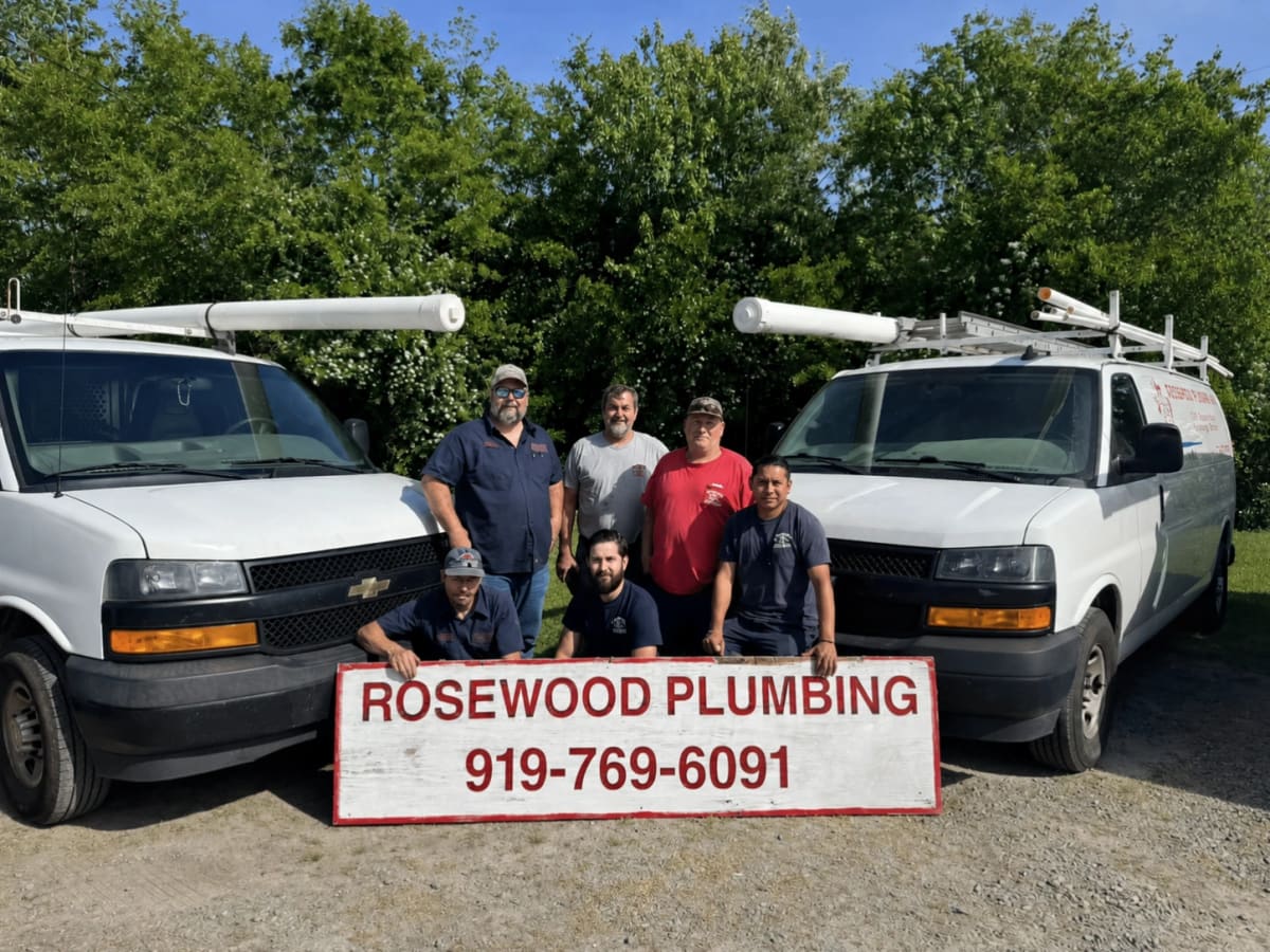 The Rosewood Plumbing crew with two service vans behind the company sign reading 919-769-6091