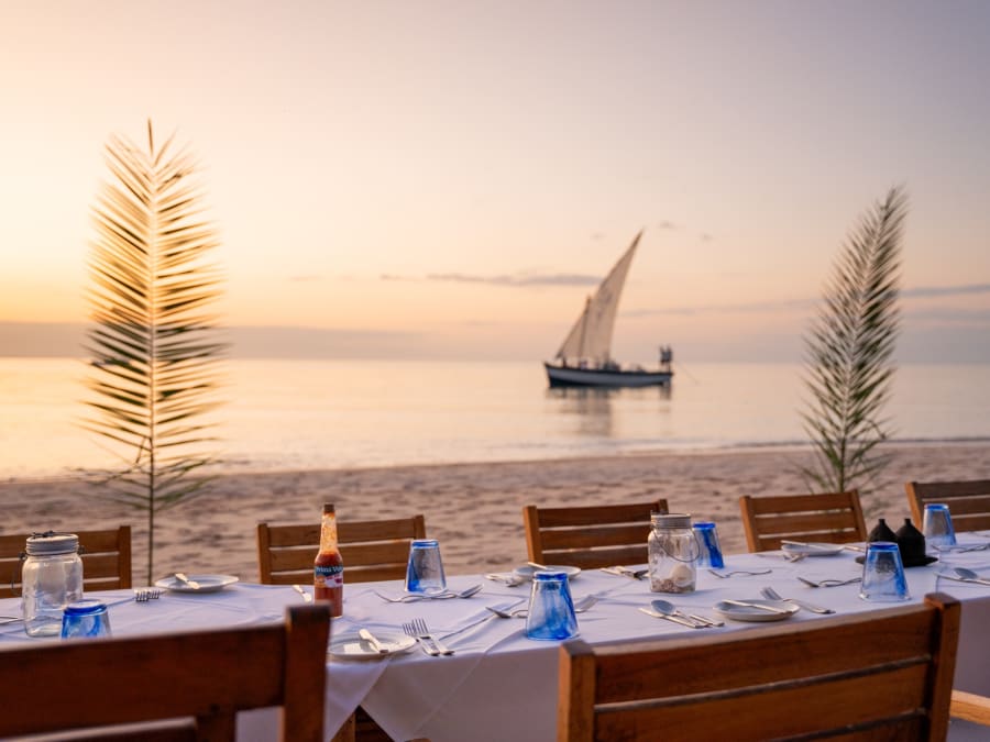 A table laid on the sand at sunset, a dhow on the water