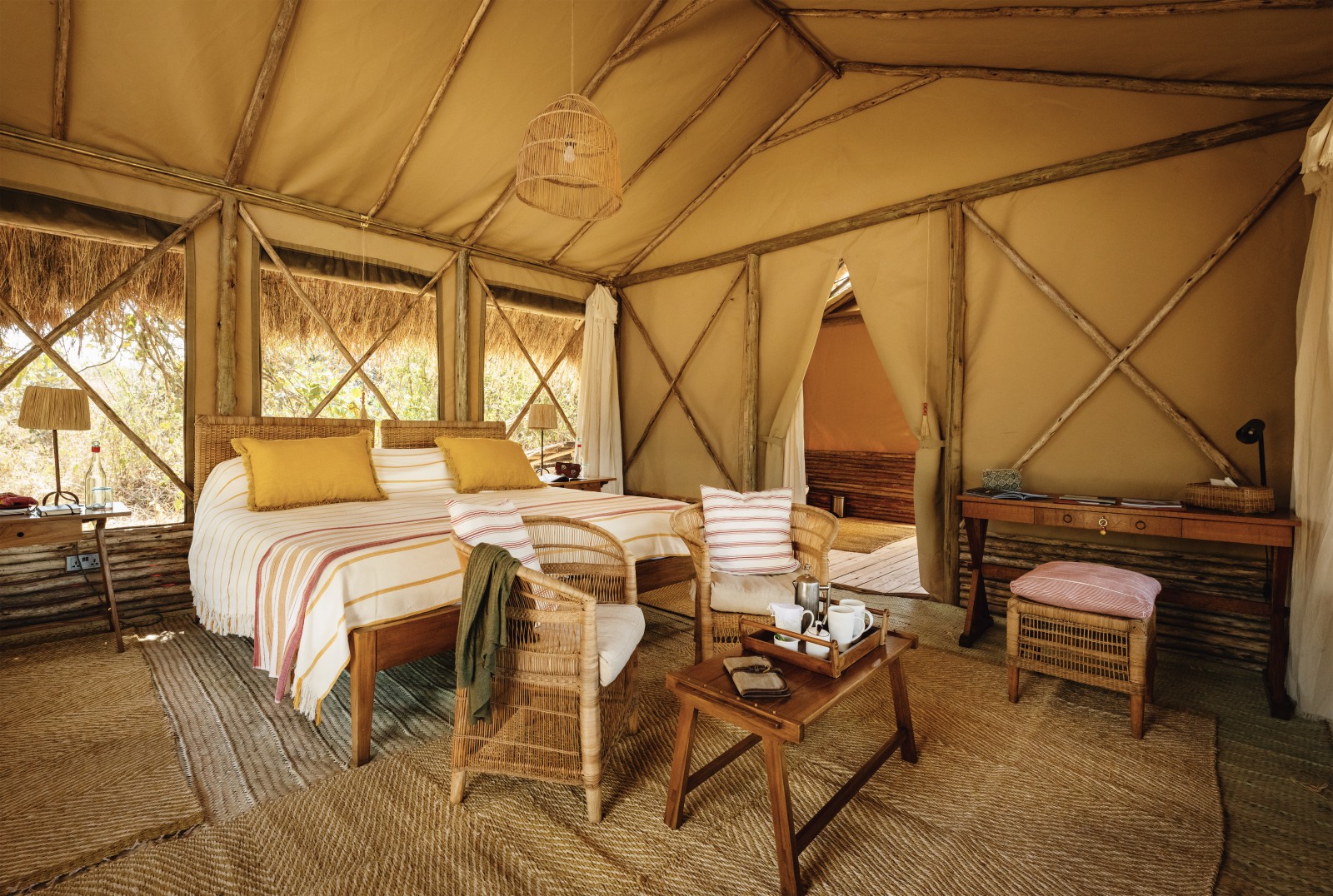 Spacious safari tent interior with a king bed, wicker chairs, and canvas walls under a thatched roof.