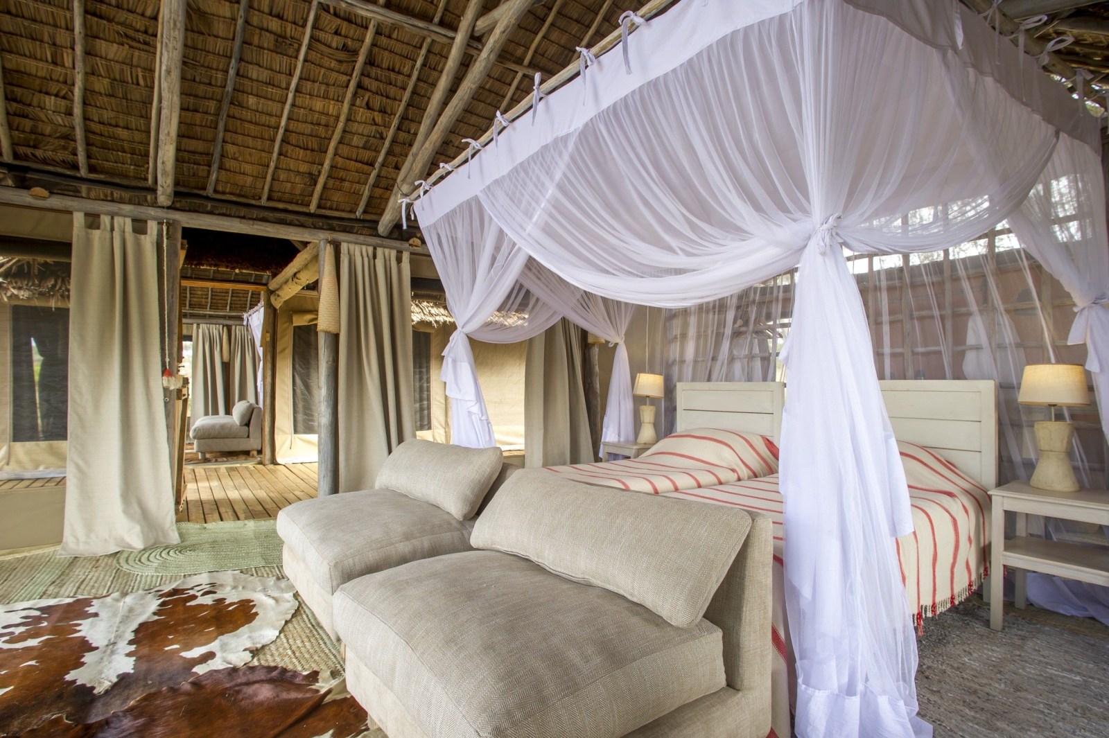 Interior of a luxury safari tent featuring twin beds with voluminous white mosquito netting and a thatched ceiling.