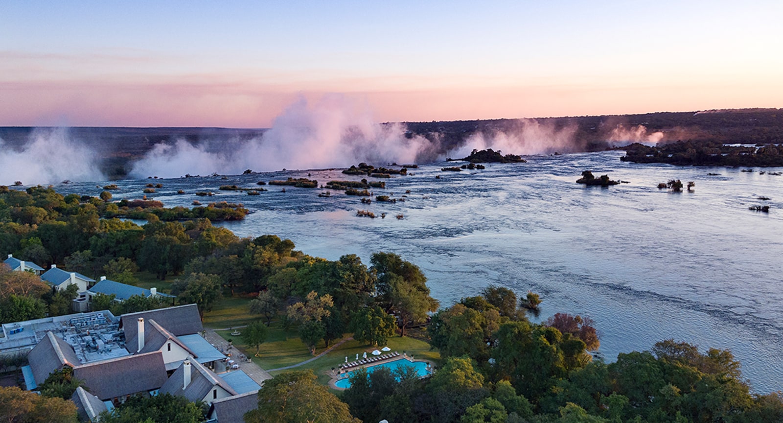 Aerial view of the hotel beside the Zambezi with the spray of Victoria Falls at sunset, The Royal Livingstone