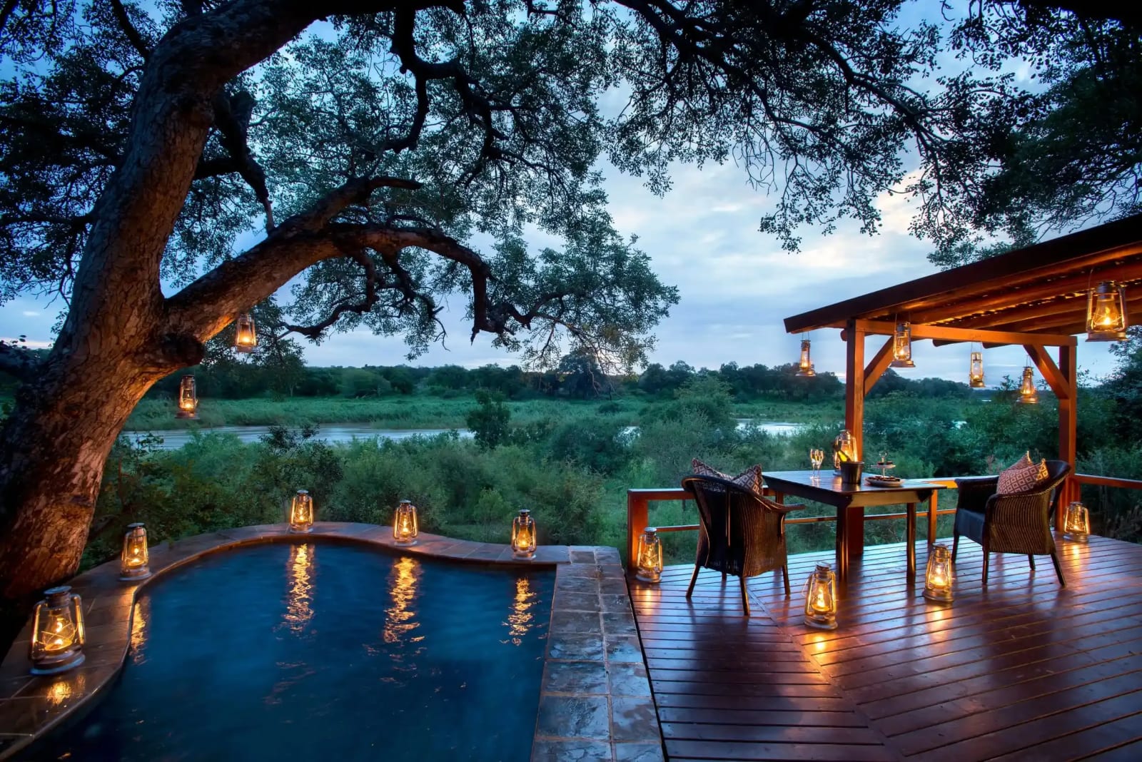 Pool and dining deck lit by lanterns above the river, Lion Sands Tinga Lodge