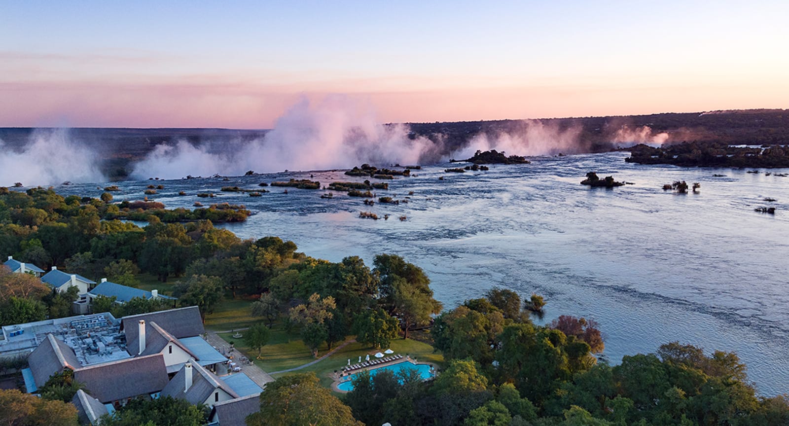 Aerial view of the hotel beside the Zambezi with the spray of Victoria Falls at sunset, The Royal Livingstone