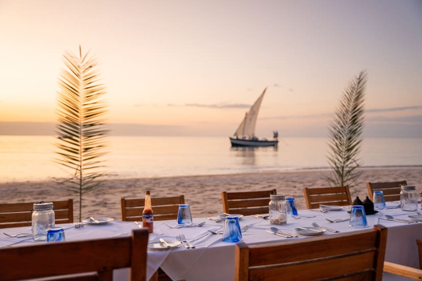 A table laid on the sand at sunset, a dhow on the water