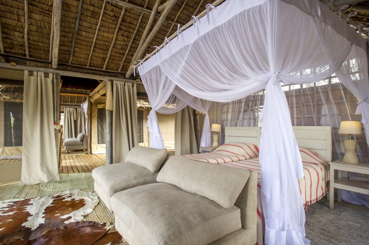 Interior of a luxury safari tent featuring twin beds with voluminous white mosquito netting and a thatched ceiling.
