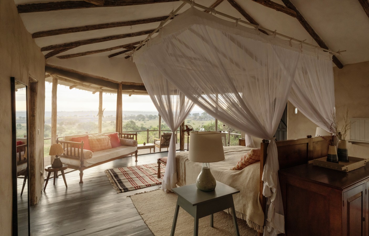 A luxury safari lodge bedroom with a canopy bed draped in a white mosquito net and a panoramic view of the savanna.