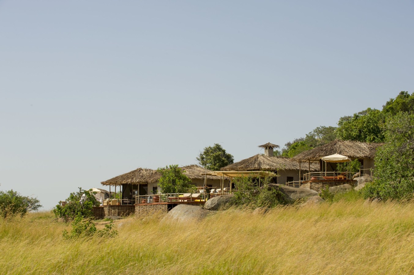 Luxury safari lodge with thatched roofs on a rocky hill overlooking golden savanna grass.