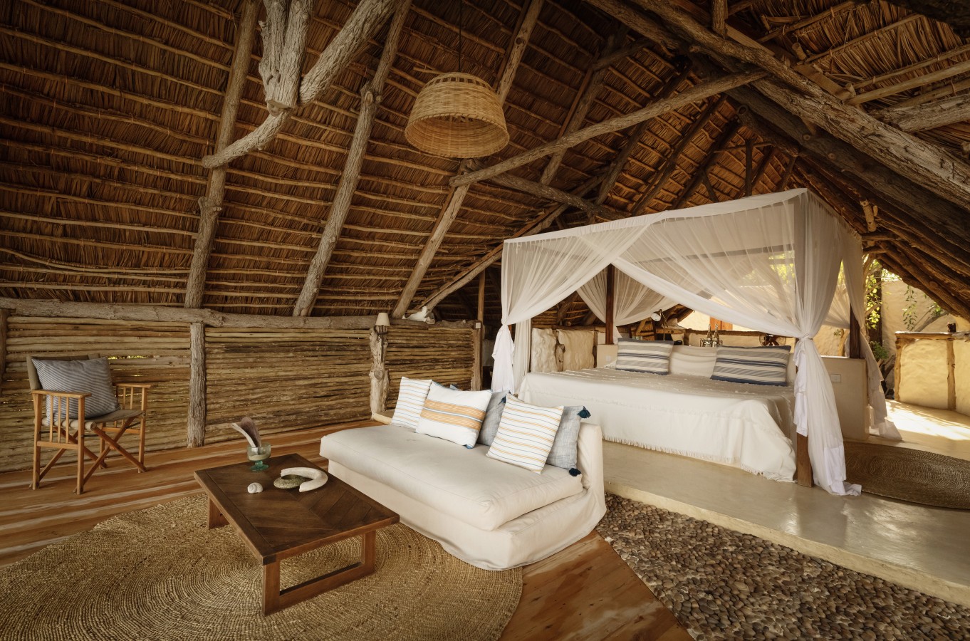 Luxury lodge interior featuring a canopy bed under a high thatched roof with rustic wooden beams.