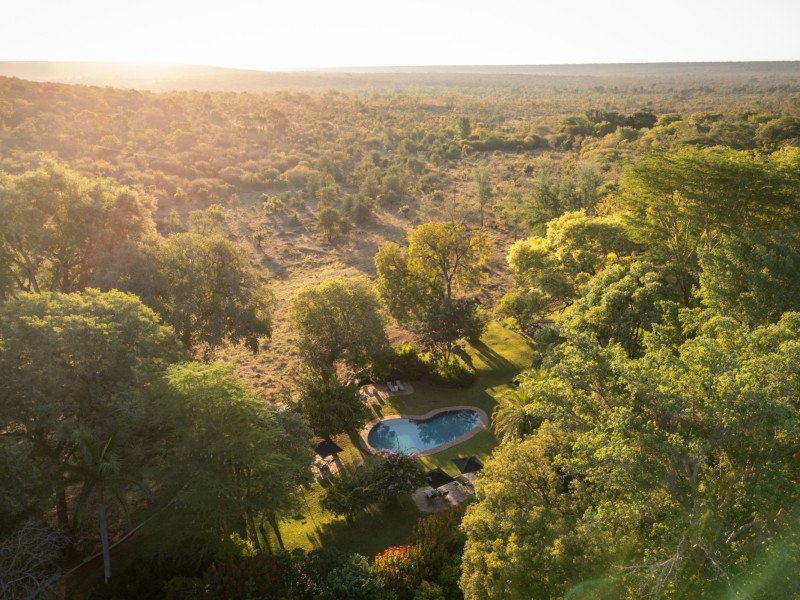 Aerial view over the private game reserve woodland in soft sunlight, with a waterhole among the trees