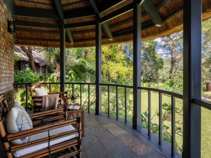 Garden View Suite veranda with wooden armchairs under a thatched roof, looking onto the garden