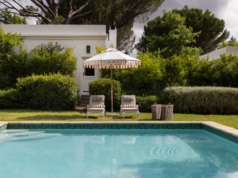 Shared swimming pool with loungers and a fringed umbrella beside the Werf Garden Cottages