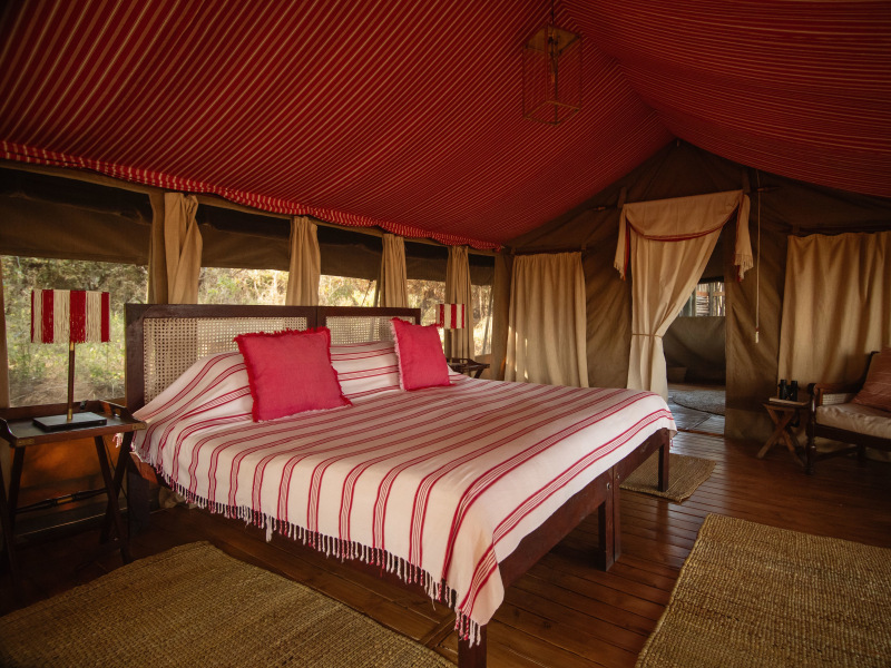 Interior of a luxury safari tent with a red and white striped bed and canopy ceiling.