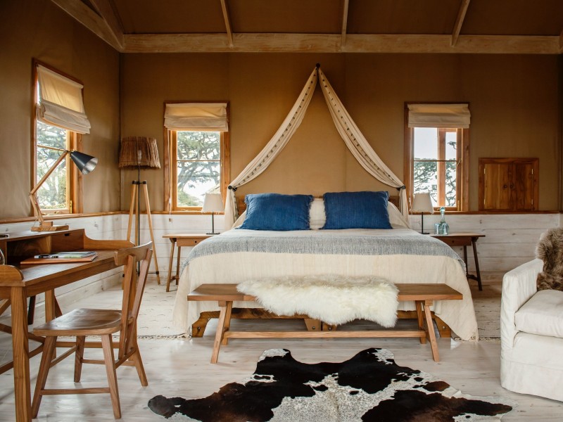 A luxurious safari tent bedroom with a large bed, wooden desk, and rustic decor.