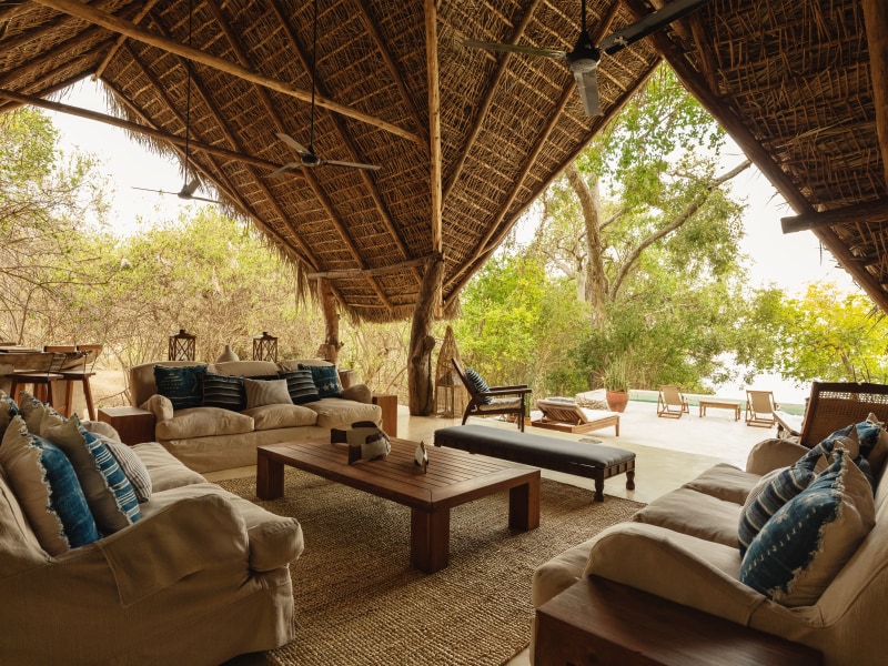 A luxury open-air safari lodge lounge with a thatched roof and comfortable sofas overlooking a forest.