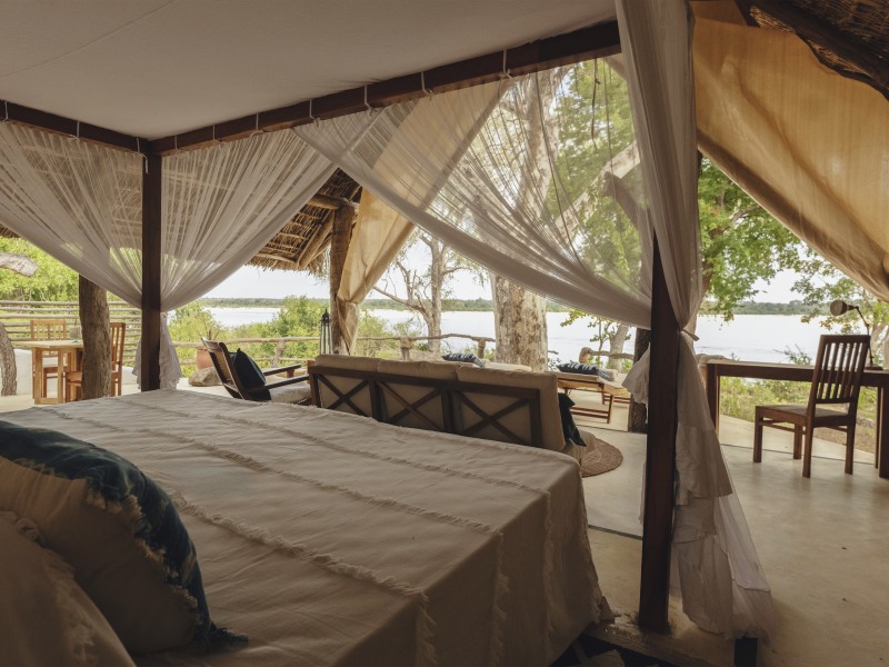 A luxury tented suite bedroom with a canopy bed overlooking a wide river landscape.