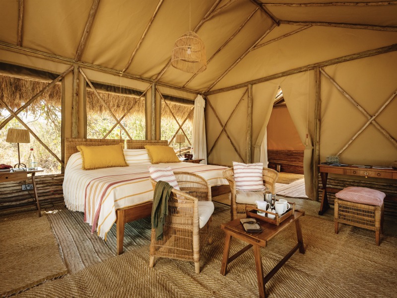 Spacious safari tent interior with a king bed, wicker chairs, and canvas walls under a thatched roof.