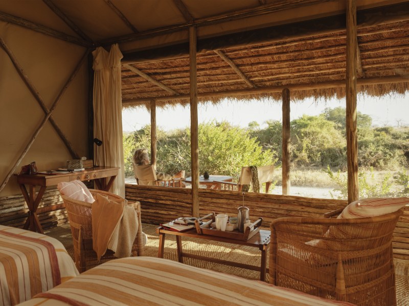 Interior of a luxury safari tent with wicker chairs, tea service, and a view of the savanna.