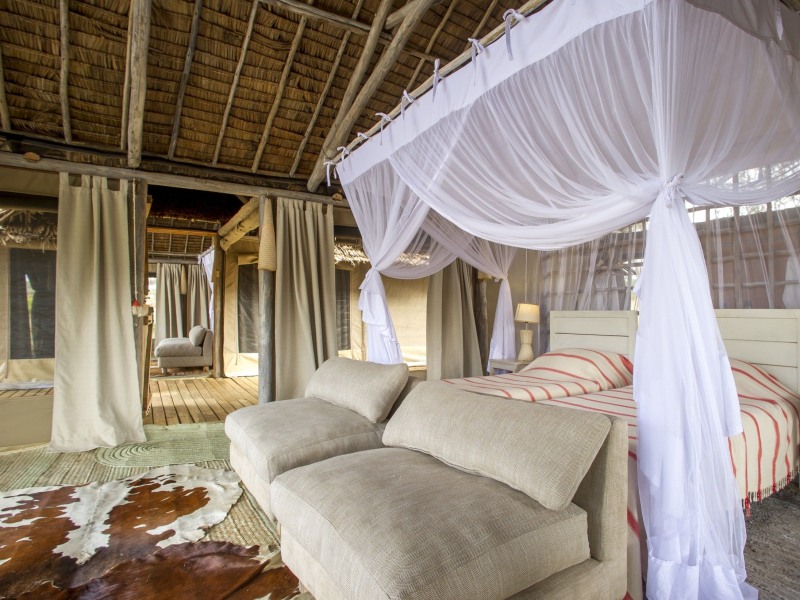 Interior of a luxury safari tent featuring twin beds with voluminous white mosquito netting and a thatched ceiling.