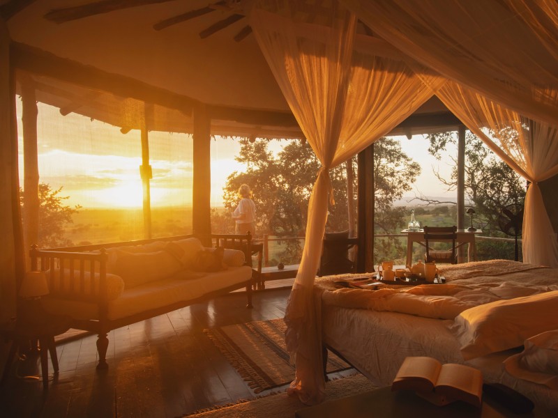 A luxury safari tent interior with a canopy bed at sunset.